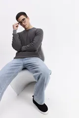 Sweater gris oscuro con textura tipo waffle y efecto acid wash, de manga larga y cuello redondo. Presenta un pequeño logo bordado en el pecho.