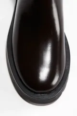 Botas Chelsea de cuero sintético color marrón oscuro (casi negro), con elásticos laterales negros y trabilla trasera. Tienen suela de goma negra con relieve y un taco bajo y ancho.