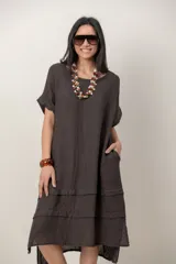 Vestido midi de lino color beige, de corte holgado y silueta acampanada. Cuenta con cuello redondo, mangas cortas amplias, bolsillos laterales y detalles de recortes horizontales en la falda con terminación asimétrica más larga en la parte trasera.