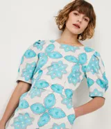 Vestido corto blanco con estampado de flores y corazones en color celeste, de corte recto, con mangas abullonadas y lazo en la espalda.