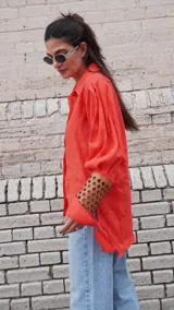 Camisa de lino color naranja, con mangas largas abuchonadas, cuello camisero y cierre frontal con botones. Presenta un diseño único con detalle calado en los puños.