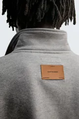 Sudadera de corte boxy fit en color gris, confeccionada en tejido de algodón con interior afelpado. Presenta cuello solapa, cierre frontal con botones a presión, manga larga con puños acanalados y bolsillo frontal tipo canguro. El bajo cuenta con un acabado elástico.