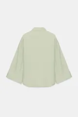 Camisa de corte oversize color marrón, con cuello solapa, mangas anchas por debajo del codo y bolsillo delantero de plastrón. Cierre frontal con botones.