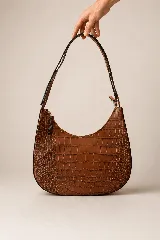 Cartera hobo de cuero marrón con textura croco y silueta curva de media luna, con correa de hombro y cierre superior.