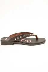 Sandalias planas de cuero marrón tipo ojota con tiras anchas adornadas con tachas metálicas plateadas y plantilla con diseño estampado.