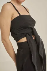Top negro con destellos brillantes, tirantes finos, escote en V pronunciado, detalle drapeado con argollas metálicas en el centro y diseño cut-out.