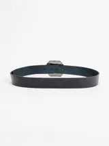 Cinto de cuero negro con hebilla hexagonal grande de metal plateado con diseño grabado y centro floral con tachas esféricas.