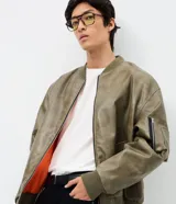 Campera bomber de poliuretano con acabado efecto cuero, cuello redondo, cierre frontal con cremallera, bolsillos delanteros y bolsillo utilitario en la manga. Presenta puños y ruedo elásticos, con forro interior en contraste.