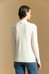 Polera de cuello alto en color blanco, confeccionada en tejido acanalado con un diseño geométrico de relieve que crea un efecto visual estilizado. Presenta un corte al cuerpo y mangas largas, ideal para usar como prenda base o principal.