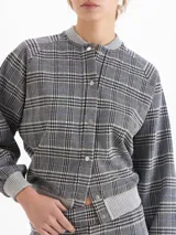 Buzo tipo bomber de tela de punto con estampado de cuadros, cuello redondo, puños y ruedo tejidos en color gris. Presenta cierre frontal con broches a presión y mangas largas con diseño holgado.