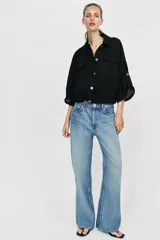 Blusa negra de cuello solapa y manga corta, con bolsillos con solapa en el pecho, bajo elástico y cierre frontal con botones.