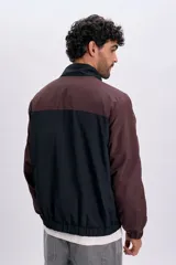 Campera estilo cortavientos en color azul oscuro, con mangas en tono marrón y detalles de líneas blancas en los hombros y mangas. Cuenta con cuello alto, cierre frontal y puños elásticos.