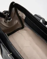 Cartera de mano de cuero sintético negro con textura granulada, doble asa superior, detalle de llavero en forma de corazón y placa metálica frontal con el logo de la marca.