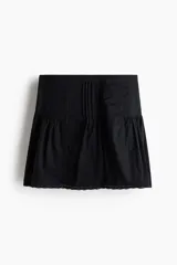 Pollera mini acampanada de algodón negro con pinzas en la parte delantera, inserciones de encaje y costuras fruncidas en la cadera con ribete de encaje en el bajo.