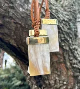 Collar con dije de nácar, ágata o cuarzo, con tiento de cuero marrón y detalles metálicos plateados.