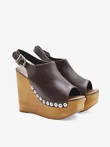 Sandalias de cuero negro con cuña alta de madera y plataforma delantera, detalle de tachas metálicas en los laterales y tira con hebilla en el talón.