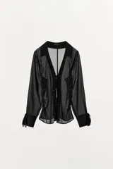 Camisa de cuello solapa con escote en pico y manga larga acabada en puño con abertura y lazo, confeccionada en tejido semitransparente de color negro con aplicación de tachas delanteras, cintura entallada con frunces laterales y cierre frontal con lazos.