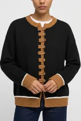 Saco tejido de punto en color negro, con detalles en color tostado en cuello, puños y ruedo. Presenta un cierre frontal con alamares y botones, y una línea blanca decorativa en los puños y el ruedo.
