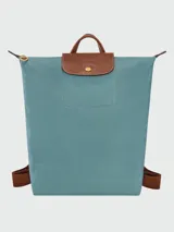 Mochila de diseño minimalista en color beige, con solapa y asa superior en cuero marrón texturizado. Cuenta con correas ajustables en color marrón y cierre principal.
