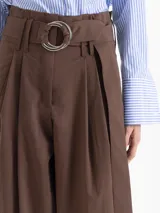 Pantalon de corte ancho y tiro alto, color marron, confeccionado en poplin elastizado. Presenta tablas en la cintura que aportan volumen, cierre frontal y un lazo ajustable con argollas metalicas.