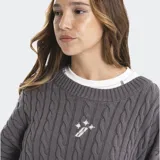 Buzo tejido de punto ochos en color gris, con cuello redondo, mangas largas y detalles de efecto roto en puños y ruedo. Presenta un pequeño logo bordado en el centro del pecho.