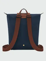 Mochila de diseño minimalista en color beige, con solapa y asa superior en cuero marrón texturizado. Cuenta con correas ajustables en color marrón y cierre principal.