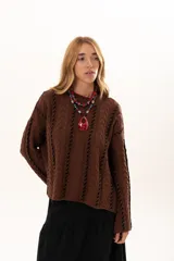 Buzo de tejido de punto color chocolate con diseño de trenzas verticales y detalles de costuras en contraste color negro. Presenta cuello redondo, mangas largas con terminación acampanada y aberturas laterales en el ruedo.