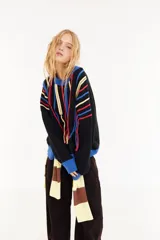 Sweater oversize de corte boxy, color crema con rayas verticales en tonos marrones y detalles de flecos colgantes. Presenta cuello redondo y puños y ruedo en tejido acanalado de color marrón oscuro.