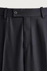 Pantalón de traje relaxed fit color negro, confeccionado en tejido con lana, con bolsillos frontales, bolsillos traseros de doble vivo con botón y raya marcada en las piernas.