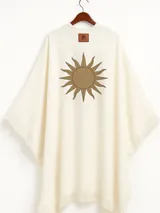 Ruana color crudo con flecos en el ruedo y estampado de un sol marrón en la espalda.