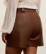 Short de cuero sintético color marrón, de tiro alto, con trabillas en la cintura, pliegues delanteros, bolsillos tipo cuchillo y cinturón para lazo.