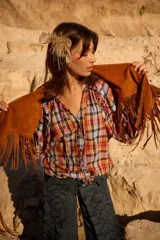 Camisa de manga larga con estampado a cuadros en tonos cálidos y azules, con volados en los hombros, cierre frontal con botones y puños elásticos. Presenta tiritas ajustables en el dobladillo para entallar la prenda.