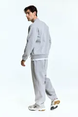 Campera bomber deportiva gris melange, de corte estándar, con cuello elevado corto, cierre bidireccional y mangas raglán. Posee bolsillos delanteros con cierre y costuras selladas, además de elástico fino en puños y bajo.