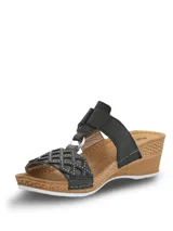Sandalia Hush Puppies de plataforma baja con diseño de tiras negras. La tira delantera presenta un patrón geométrico calado con pequeñas tachas metálicas, mientras que la tira superior cuenta con un cierre de velcro para un ajuste personalizado. La plantilla es de color marrón y la suela tiene un acabado texturizado que simula madera.