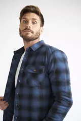Sobrecamisa de viyela para hombre con estampado de cuadros en rojo y negro. Presenta cierre frontal con botones, bolsillos en el pecho con solapa y botón, y un interior capitoneado para mayor abrigo. Cuenta con un logo en grifa de cuero.