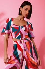 Top de crepe con estampado geométrico abstracto en tonos rosa, rojo, verde y naranja. Cuenta con escote cuadrado, mangas cortas ligeramente acampanadas y corte crop con diseño estructurado en el bajo.