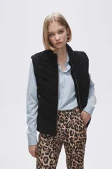 Chaleco negro capitoneado sin mangas con cierre frontal dorado.