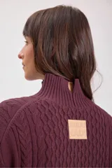 Sweater de punto color bordó con cuello alto y diseño de trenzas en el frente y las mangas. Presenta un corte holgado y largo, con puños y ruedo acanalados.