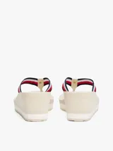 Sandalias tipo ojota con plataforma de cuña alta, color beige claro. Las tiras son de tejido trenzado con las franjas distintivas de Tommy Hilfiger (azul marino, blanco y rojo).