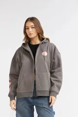 Campera de felpa gris con cierre frontal completo, capucha con cordón ajustable y bolsillos frontales tipo canguro. Presenta diseño holgado, hombros caídos y detalles estampados en rosado en el pecho y la manga.