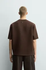 Sudadera de manga corta con corte relajado, confeccionada en tejido técnico compacto de algodón con elasticidad. Presenta cuello redondo y detalle de tacha metálica en la espalda.