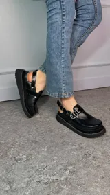 Zuecos negros de cuero con plataforma baja de 3 cm, detalle de argolla metálica, tiras laterales y tira trasera con hebilla regulable.