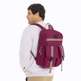Mochila urbana Merrell en color bordó, confeccionada en lona de poliéster. Presenta un compartimento principal con cierre de doble cursor, dos bolsillos frontales con solapa y correas de ajuste en color beige con hebillas de liberación rápida. Incluye un parche frontal con el logo de la marca y una cinta decorativa horizontal.
