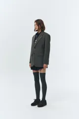 Blazer de lana color gris oscuro, con cuello sastre, cierre frontal de dos botones y hombreras. Presenta parches de ante sintético en los codos y un calce relajado tipo overfit.