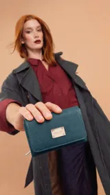 Billetera corta de símil cuero con cierre de broche a presión. Presenta una placa metálica decorativa con el logo de la marca en la parte frontal. El interior incluye tarjeteros, visor y compartimentos para billetes, además de un bolsillo posterior con cierre.