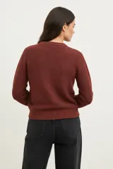 Sweater de poliéster color bordó, con cuello redondo, manga larga y diseño holgado. Presenta un patrón de punto trenzado en forma de chevrón en la parte frontal.