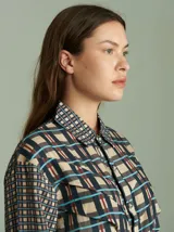 Camisa de viscosa con estampado a cuadros de estilo retro en tonos beige, azul marino, celeste y rojo. Presenta cuello camisero, cierre frontal con botones metálicos plateados y diseño con capas superpuestas en el pecho de inspiración country.