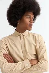 Camisa de manga larga color crema, con cuello clásico y botones blancos frontales.