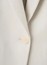 Blazer sastre entallado color beige, con cuello en pico, solapas de muesca, manga larga y bolsillos con solapa en la parte delantera.