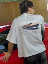 Remera celeste de corte recto con estampado de un yate y texto en color gris.